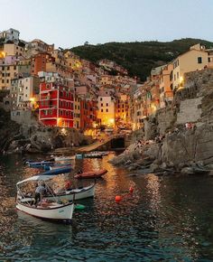 several boats are docked on the water in front of some buildings and cliffs at night