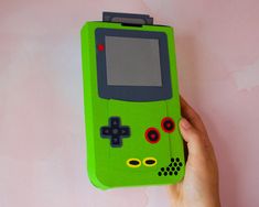 a hand holding a green gameboy case with red and black buttons on the front