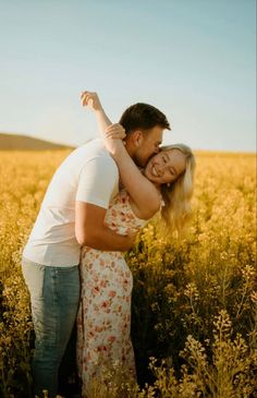 a man and woman hugging in a field of tall grass with the sun shining on them