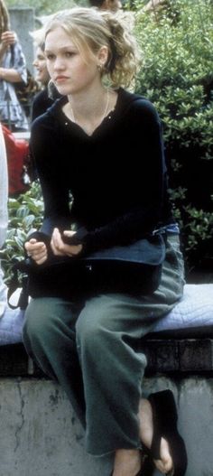 a woman sitting on top of a cement bench next to another woman with her hands in her pockets