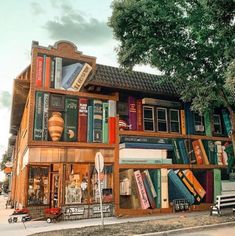 a building made out of books on the side of a street in front of a tree