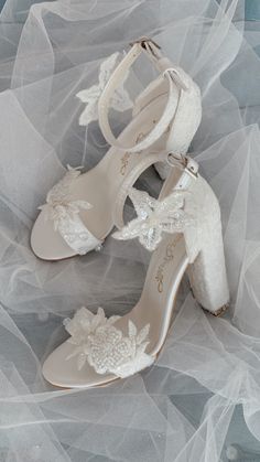 two pairs of wedding shoes with white lace and flowers on the toes, sitting on a bed of tulle