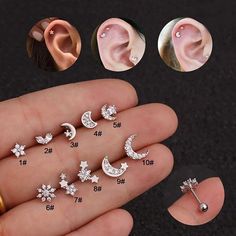 six pairs of moon and stars piercings in different shapes, sizes and colors on a person's hand