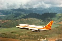 an orange and white airplane is flying over the mountains in front of some green fields