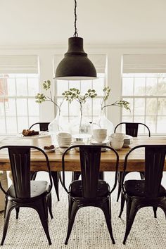 a dining room table with four chairs and two vases on top of the table