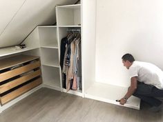 a man kneeling down in front of a closet with clothes on hangers and drawers