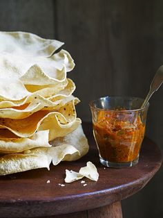 a stack of tortillas with salsa on the side next to a glass cup