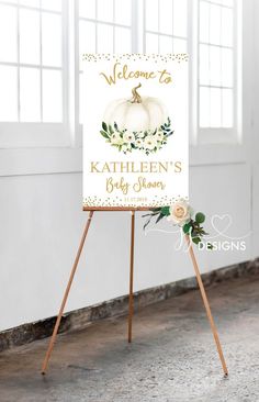 a welcome sign for a baby shower is displayed in front of a white door with greenery and pumpkins