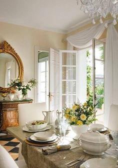 a dining room table is set with plates and silverware, flowers in vases, and a chandelier