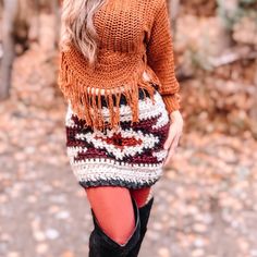 a woman wearing boots and a sweater is standing in front of some trees with her hands on her hips