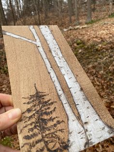 someone holding up a piece of wood with trees on it