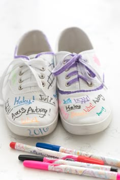 two pairs of white shoes with writing on them next to three markers and one ballpoint pen