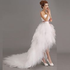 a woman in a white dress with feathers on the skirt and heels is posing for a photo