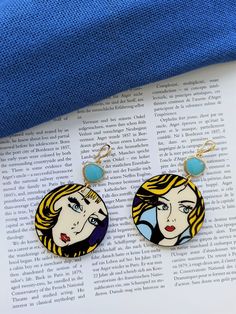 two earrings are sitting on top of an open book, one is blue and the other has