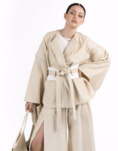 A loose-fitting jacket with detachable sleeves made from linen. The design features a round neckline, convenient pockets, and a double belt: one wide and one narrow. Thanks to the detachable sleeves, the jacket can be worn as a vest. The stitching and accent sleeves give the piece an Asian-inspired look. The jacket is available in a one-size-fits-all.Product details: Back length from the waist: 62 cm / 24,4 in Sleeve length: 57 cm / 22,4 in Model: height 178 cm / 70 in; bust: 88 cm / 34,7 in; waist: 63 cm / 24,8 in; hips: 93 cm / 36,6 in; wearing size: OS Season: Spring / Summer / Autumn Composition: 74% Cotton 23% Linen 3% ElastanCare instructions: Machine wash at 30°C. Spin: 600-800 rpm. Do not use the drying mode in the washing machine. Do not use chlorine bleach or stain removers. Iron Autumn Composition, Stain Removers, Linen Kimono, Double Belt, Detachable Sleeves, Asian Inspired, Luxury Shop, Model Height, Cloth Bags