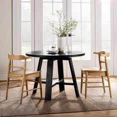 a black table with two chairs and a vase on the top, in front of three windows