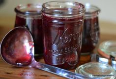 three jars filled with jam sitting on top of a wooden table next to a spoon