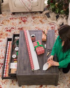 a woman sitting on the floor next to a coffee table with wrapping and scissors in it