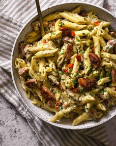 a bowl filled with pasta and sausage on top of a striped table cloth next to a fork