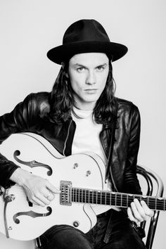 a man with long hair wearing a black hat and holding a white guitar in his hands