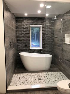 a white bath tub sitting next to a toilet in a bathroom under a large window