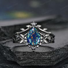 a ring with an opal stone in the center and leaves around it, sitting on top of a rock