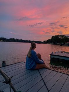 a woman sitting on top of a wooden pier next to a body of water at sunset