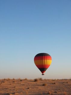 a hot air balloon flying in the sky over a desert area with sparse grass and sand