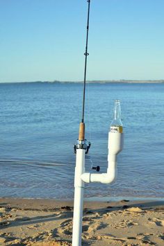 a white pipe with a fishing rod attached to it sitting on the beach next to water