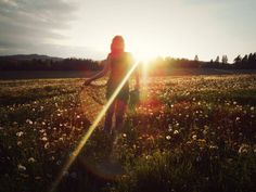 a woman standing in a field with the sun shining behind her and holding a basket