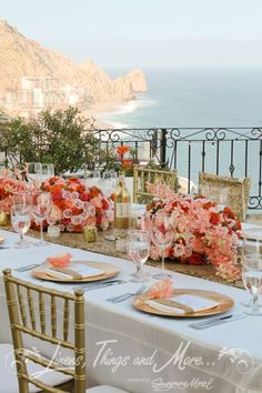 a table set up with flowers and place settings for an outdoor dinner overlooking the ocean