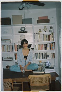 a woman sitting at a desk in front of a book shelf with books on it