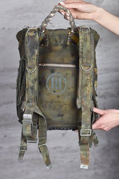 Post Apocalyptic Bag - Postapoc Backpack - Military Rucksack - Camouflage Package - Wasteland Weekend - Burning Man - LARP Accessory Pack Get ready for the post-apocalyptic world with this military green backpack made from waterproof army canvas.  Adorned with yellow biohazard stripes, skulls, and chains, this backpack is perfect for those with a unique sense of style. It features two side pockets, two pockets under the flap, and a drawstring main compartment. There's also a small zipper pocket at the back for added security. With plenty of attachment points, you can easily carry everything you need for your next adventure. Whether you're exploring a desolate wasteland or just commuting to work, this backpack is sure to turn heads. The backpack has a reinforcement at the back and has a spe Punk Style Backpack With Adjustable Strap, Military Style Backpack For Adventure, Punk Style Backpack For Everyday Use, Punk Style Standard Backpack For Everyday Use, Alternative Style Everyday Backpack, Punk Style Travel Backpack, Punk Style Standard Travel Backpack, Durable Backpack For Streetwear, Alternative Style Backpack For Everyday Use