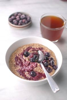 a bowl of oatmeal with blueberries in it next to a cup of tea