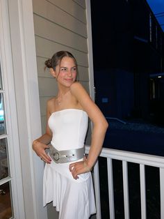 a woman in a white dress standing on a porch with her hands on her hips