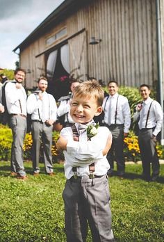 a little boy standing in front of a group of men wearing ties and vests