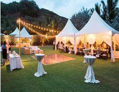 an outdoor event with tables and chairs set up under white tented tents at night