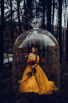 a woman in a yellow dress standing under a glass dome with flowers on the ground