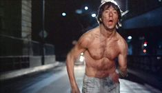 a shirtless man running down the street at night with his mouth open and tongue out