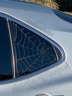 a silver car with a spider web on it's side window and its reflection