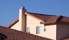 a tan house with red tile roof and white shutters