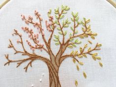 a tree with leaves and flowers is embroidered onto a white fabric piece in a hoop