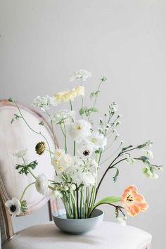 white flowers are in a blue bowl on a table next to a mirror and chair