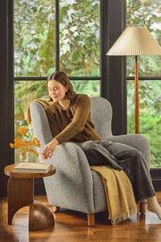 a woman sitting in a chair with a book on her lap looking out the window