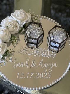 a wedding cake decorated with white roses and two small lanterns on top of it,