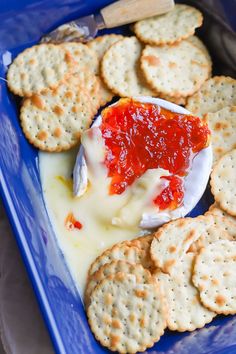 crackers, cheese and jelly are on a blue plate with a spoon in it