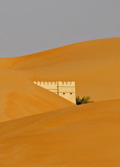 a white building sitting on top of a sandy hill in the middle of sand dunes