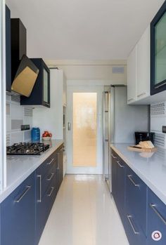 a long narrow kitchen with blue cabinets and white counter tops, along with an open door leading to the outside