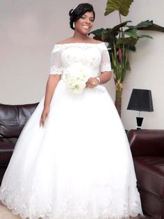 a woman in a white wedding dress standing next to a couch