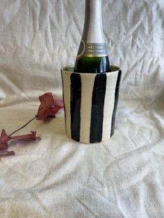 a black and white striped cup with a wine bottle in it on a white sheet